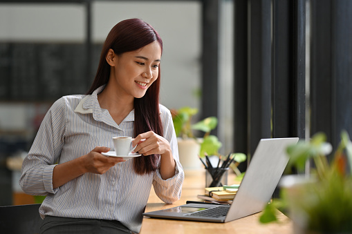 Asian Businesswoman working with laptop while holding a cup of coffee in the cafe.