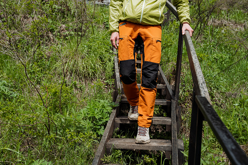 Legs in orange pants go down the steps. A man walks in tourist shoes on wooden steps, the railing held by hand. High quality photo