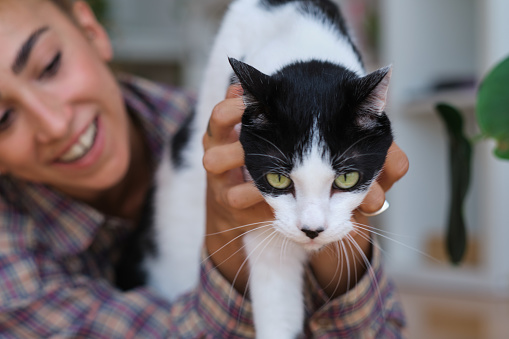 side view portrait of a Latino generation Z woman smiling and having a beautiful moment with a black and white feline indoors