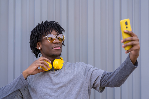 African cool man taking a selfie next to a urban grey wall