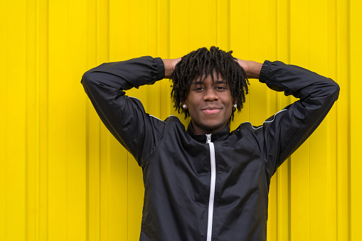 Smiling young african man posing relaxed outdoors next to an urban yellow background