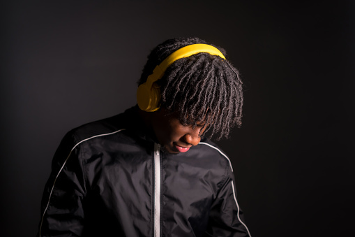 Dark studio portrait of a distracted young african man listening to music with headphones