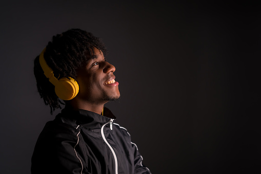Dark studio portrait of a young african man listening to music with headphones