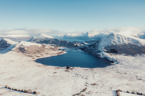 Drone panoramic photo of the beautiful snowcapped mountain range with background view of the big lake with the cold sea during cold winter season in the western fjords of Scandinavia