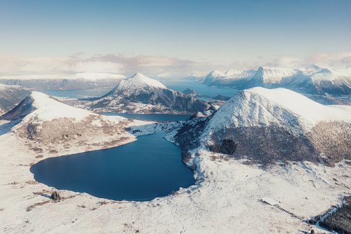 Drone panoramic photo of the beautiful snowcapped mountain range with background view of the big lake with the cold sea during cold winter season in the western fjords of Scandinavia