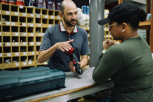 male owner of a hardware store explaining parts of a drill to a customer - sales clerk store manual worker retail imagens e fotografias de stock