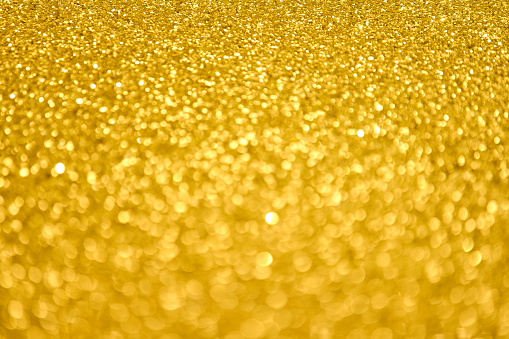 Defocused golden sequin light. Fancy gold glitter sparkle background. Studio shooting of a creative bright yellow color background. It is textured color gradient. There are no text and no people, and have copy space for design. Its Suitable for commercial use. Christmas, New Year, Diwali festive celebrations themed backgrounds, wallpapers, templates for greeting cards, banners and posters and wrapping paper is apt.