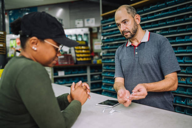 male owner of a hardware store giving a customer advice on screws - sales clerk store manual worker retail imagens e fotografias de stock
