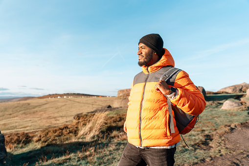happy handsome man tourist with backpack hiking and enjoying mountains landscape at sunset in England. A trip to the mountains with a backpack. Enjoy hiking and exploring new places concep