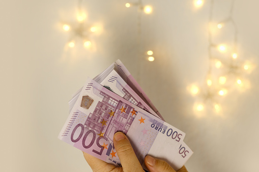 female hand holds cash 500 euro banknotes on blurred creamy background with bokeh, salary, payments to fund, gift for holiday, social assistance to poor, save up for vacation, car, winnings in casino