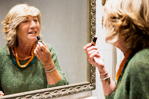 Mature woman making up her lips in front of the bathroom mirror