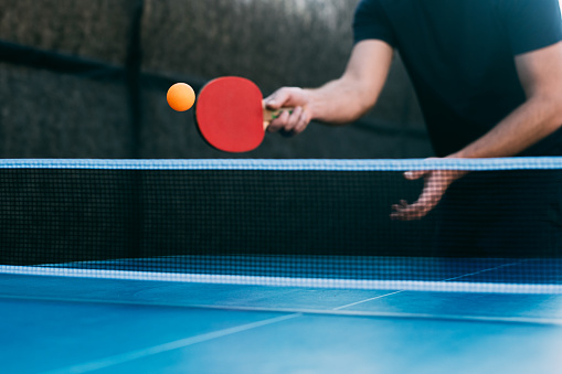 View of a young man playing table tennis. He just made a shot with a table tennis racket and ball is in motion. Copy space.