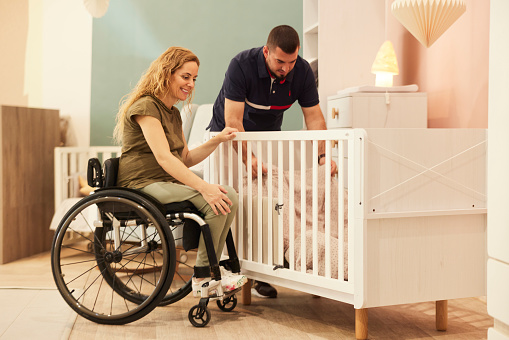 Expectant parents, with the wife in a wheelchair, shop for baby crates, sharing the excitement of preparing for their newborn.