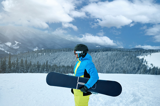 Portrait of man at  ski resort on the background mountains holds snowboard. Wearing ski glasses