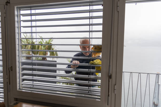 Mature man cleaning window blinds on an apartment balcony