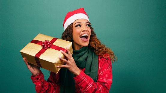 Excited young woman shakes Christmas gift, guessing what is inside, Studio. High quality photo