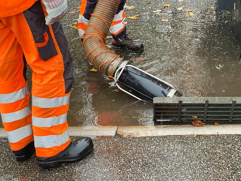Two individuals are laboring to unclog a drain that became obstructed following a substantial rainfall