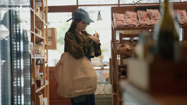 Young asian woman use reusable bag and looking at various products in eco friendly store.