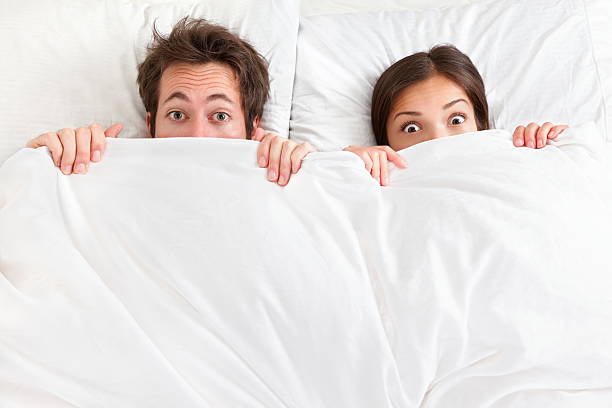 funny couple au lit - hiding fear men peeking photos et images de collection