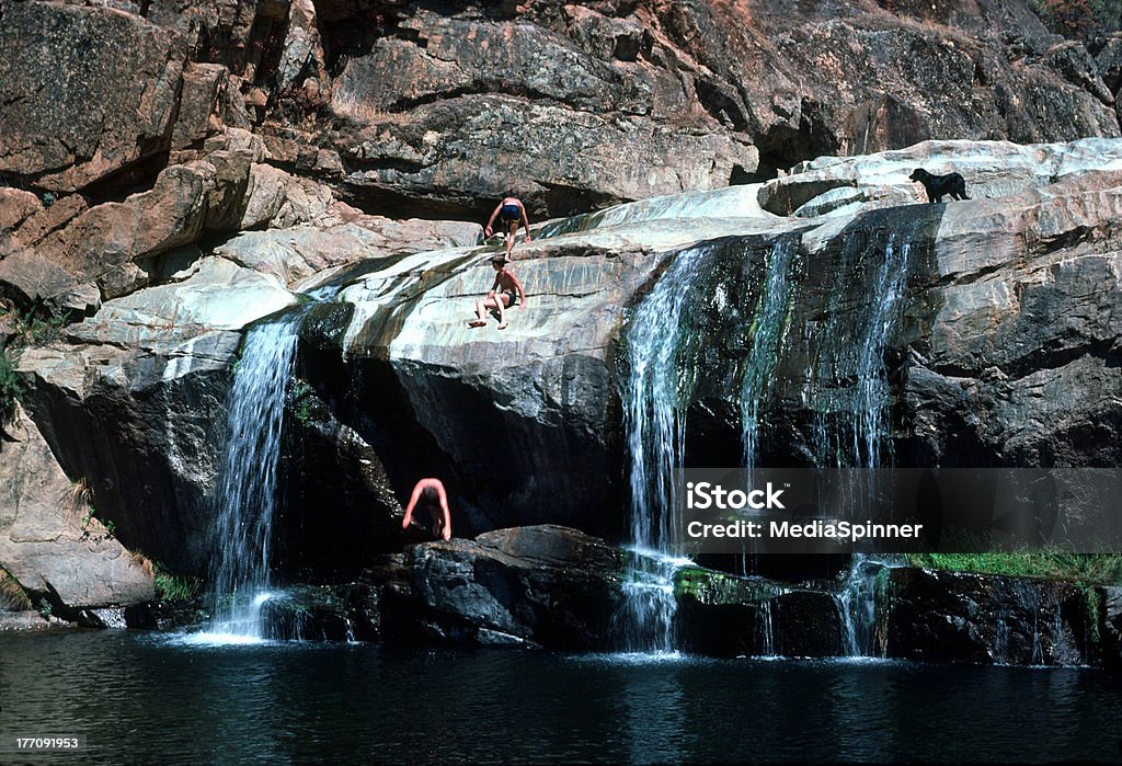 Boys Dive Into Swimming Hole Three boys and a dog enjoy a beautiful swimming hole with waterfalls and plenty of sunshine.  Richly colored rocks and water show off in this 35mm Kodachrome film scan. Cliff Diving Stock Photo
