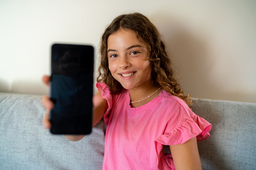 Happy teenage girl sitting on sofa and showing smartphone screen