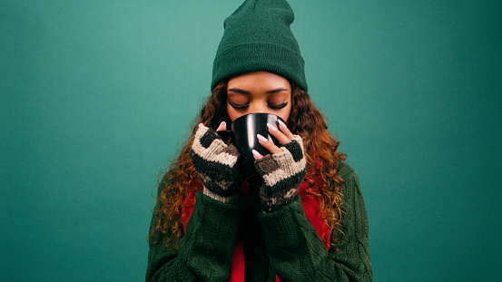 Beautiful young woman sips warm drink in winter, Christmas colours studio. High quality photo