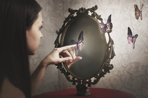 woman surprised by her exit from her mirror of surreal butterflies; ; concept of introspection and freedom