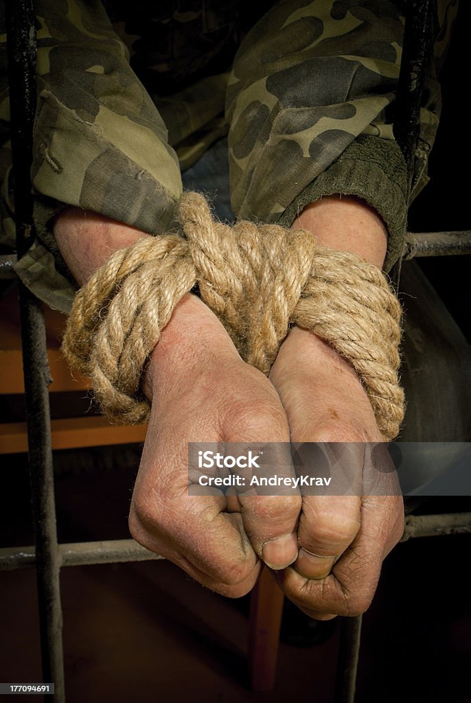 Man with hands tied up Man with hands tied up with rope behind the bars Behind Stock Photo