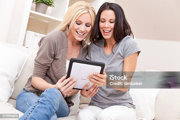 Two Young Women Using Tablet Computer At Home On Sofa Stock Photo - Download Image Now