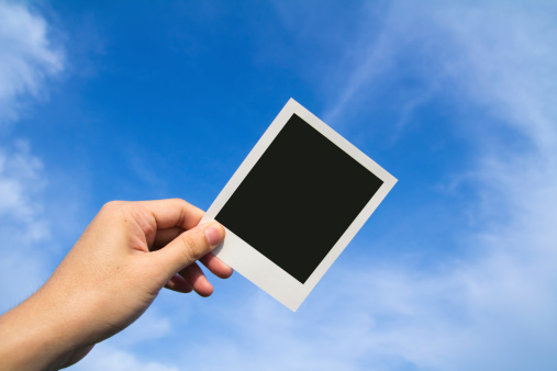 Hand holds a polaroid photo frame against blue sky