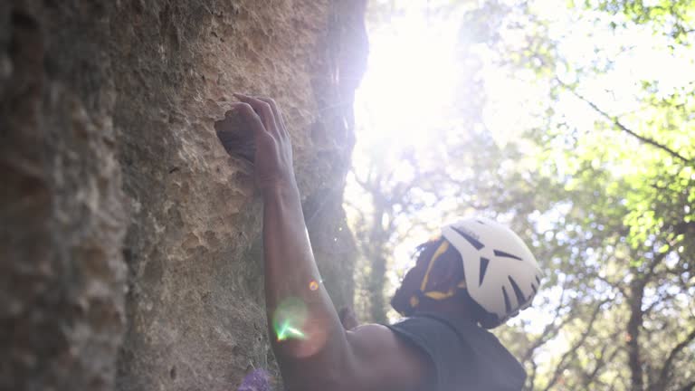 Close-up of an athletic climber holding onto a rock ledge with a helmet and lens flare.