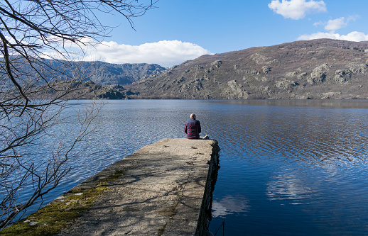 Postcard image of a young man sitting on a footbridge on the shores of Lake Sanabria in the province of Zamora - Castilla y León - SpainMan on the shore of a lake.Young man sitting looking at the landscape of a lake in the province of Zamora - Castilla y León - Spain - Lake Sanabria -
middle-aged man gazes at the largest glacier in Europe - wearing a maroon plaid shirt - Lonely young man meditates on the shore of a glacier. Spain