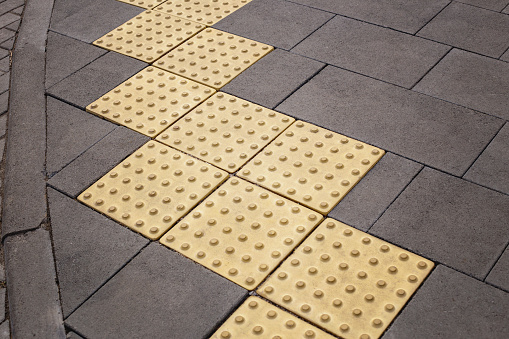 Tactile pavement or braille blocks on the sidewalk on a city street in front of a crosswalk. Tile for the visually impaired, textured surface indicator. The concept of care for the disabled, inclusiveness
