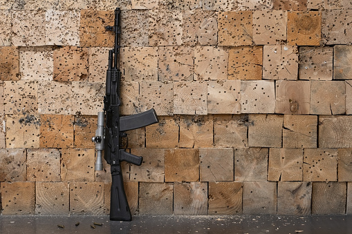 Rifle with old fashioned optical sight against the wooden wall in a shooting range, side view