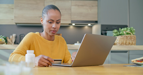 Woman holding credit card while using laptop in kitchen.