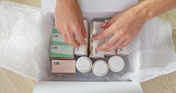 Overhead view of man's hand removing medicines from pharmacy box.