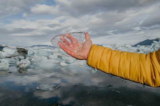 Male hand in yellow jacket holding black piece of ice in the glacier lagoon in Iceland