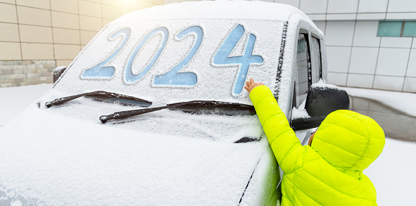 Young boy with new year number 2024 written on car windshield