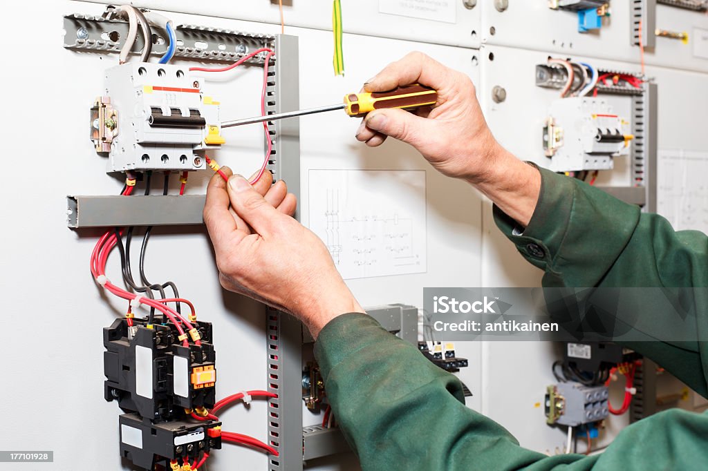 Worker's hands with screwdriver working on electric panel Electrician working in electrical shield with an electric screwdriver. Electricity Stock Photo