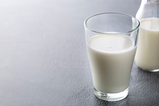 Splashes of milk in a glass on a white surface. Milk is poured into the glass infront of a white wooden background.