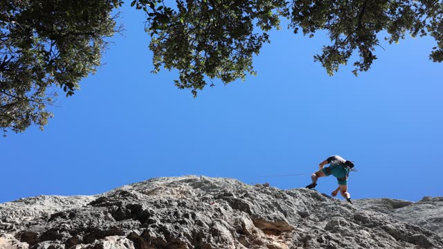 Athletic man jumping and rapelling rock with climbing rope and carabiners.