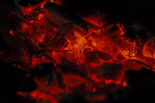 Red hot coal bars in focus on dark background with flames. Background of raw coal with soft focus exclusion with color and temperature.