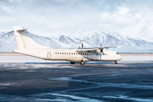 weißes passagier-turboprop-flugzeug auf dem winterlichen flughafenvorfeld vor dem hintergrund hoher malerischer berge - airfield mountain snow airport stock-fotos und bilder