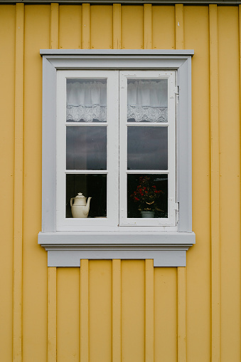 Kettle and plant in the window of a yellow painted house