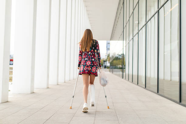 A mid adult woman with crutches carrying a sack walkingdown the outside corridor in urban scenery next to office building