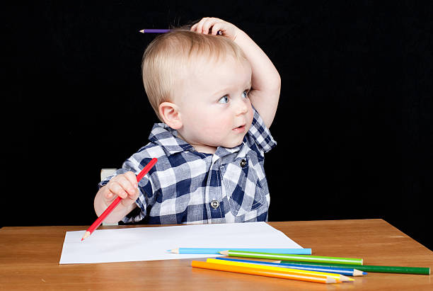 Young boy sitting at desk with pencils drawing stock photo