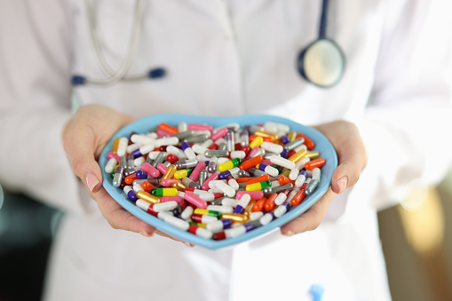 Doctor in medical uniform holds heart-shaped plate with colorful pills in hands. Dietary supplements capsules for improving health and body condition