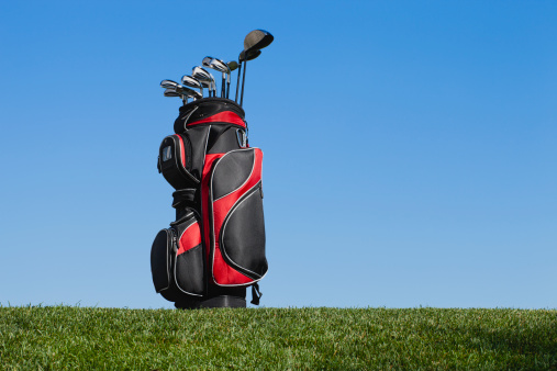 Side view of golf clubs in a red and black bag on green grass against a blue skyMore golf images: