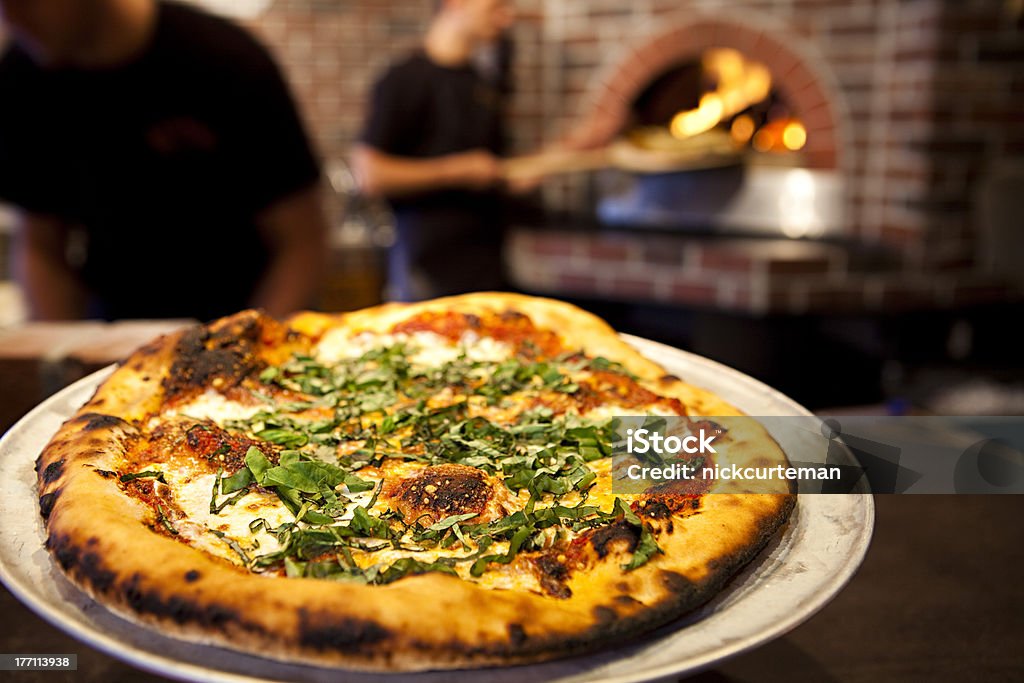 Wood fired pizza Workers preparing and presenting a margarita pizza from a wood fired brick oven. Pizza Stock Photo