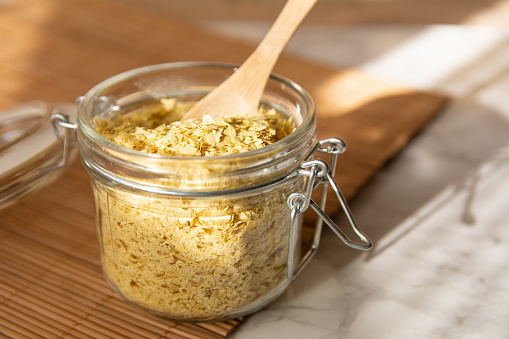 Closeup of Nutritional yeast in a glass jar with wooden spoon. Cheese substitute